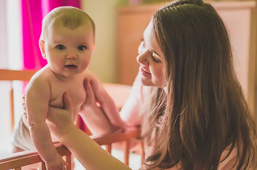 Mãe sorridente interage com bebê que está de pé no berço. - Mustela Brazil - 1
