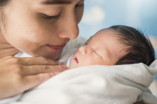 Mãe olha tranquilamente para seu bebê recém-nascido que está no seu colo dormindo. - Mustela Brazil - 1