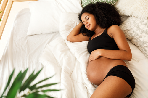 Mulher grávida deitada em uma cama confortável, sua mão está sobre a barriga e sua expressão é de relaxamento. - Mustela Brazil - 1
