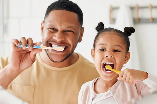 Pai e filha escovando os dentes em frente a um espelho. - Mustela Brazil - 1