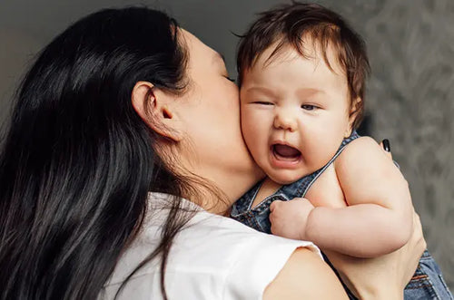 Mãe segurando um bebê e dando um beijo em sua bochecha. - Mustela Brazil - 1