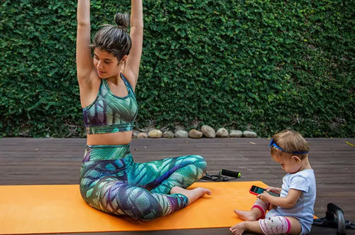 Mulher em cima de tapete de ginástica se alongando e bebê ao lado. - Mustela Brasil - 1