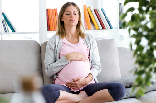 Grávida sentada em um sofá, com as mãos ao redor da barriga e expressão relaxada. - Mustela Brasil - 1