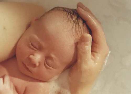 Bebê recém-nascido no colo de sua mãe, dorme relaxado enquanto ambos estão em uma banheira com água e espuma. - Mustela Brasil - 1