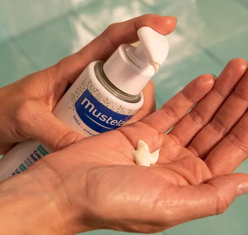 Uma mão apertando o produto Stelatopia+ e deixando cair uma gota do produto na outra mão. - Mustela Brasil - 1