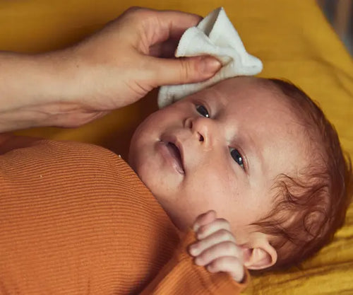 Mão limpando delicadamente o rosto de um bebê que está tranquilamente deitado. - Mustela Brasil - 1