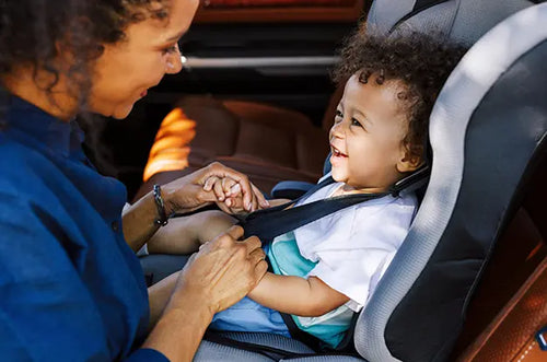 Mãe ajusta cinto da cadeirinha no bebê sorridente dentro de um carro. - Mustela Brasil - 1
