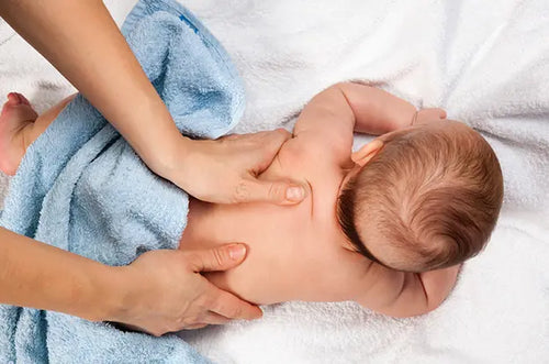 Bebê deitado de bruços em uma cama recebendo massagem nas costas. - Mustela Brasil - 1