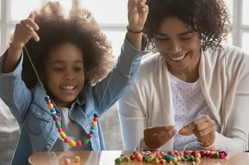 Mãe e filha brincam juntas montando colar com miçangas. - Mustela Brasil - 1