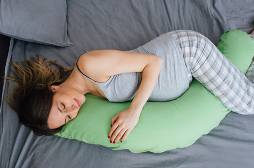 Mulher grávida deitada na cama abraçando um travesseiro longo. - Mustela Brasil - 1