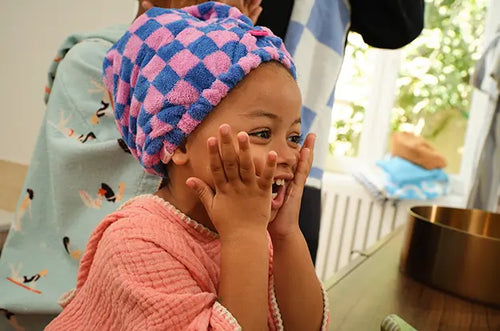 Menina sorridente passando hidratante no rosto. - Mustela Brasil - 1