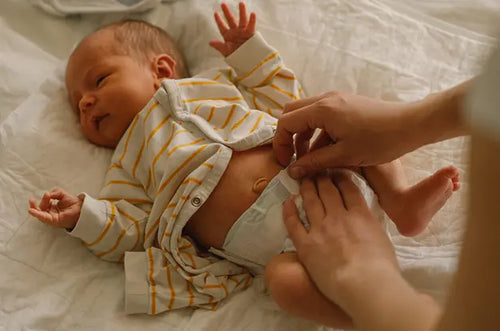 Bebê recém-nascido deitado em cama. Uma pessoa está trocando sua fralda. - Mustela Brasil - 1