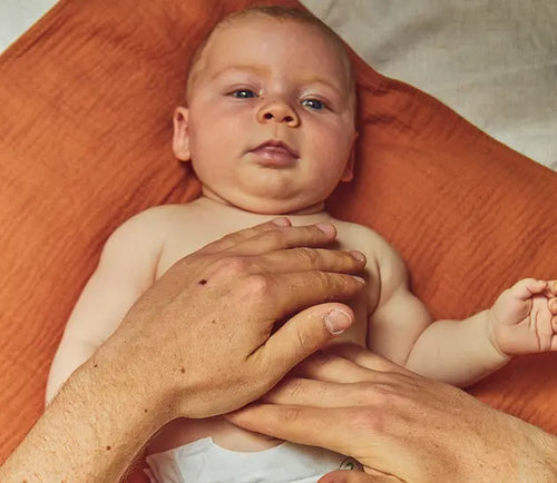 Bebê deitado tranquilo em almofada recebendo massagem na barriga. - Mustela Brasil - 1