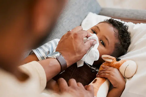 Bebê deitado e seu pai usando um lenço para assoar seu nariz. - Mustela Brasil - 1