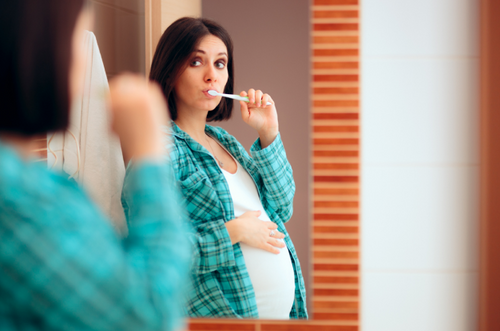 Mulher grávida escovando os dentes e se olhando no espelho. - Mustela Brasil - 1