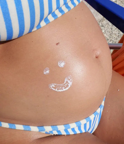 Grávida de biquini com um sorriso desenhado com protetor solar na barriga. - Mustela Brasil - 1