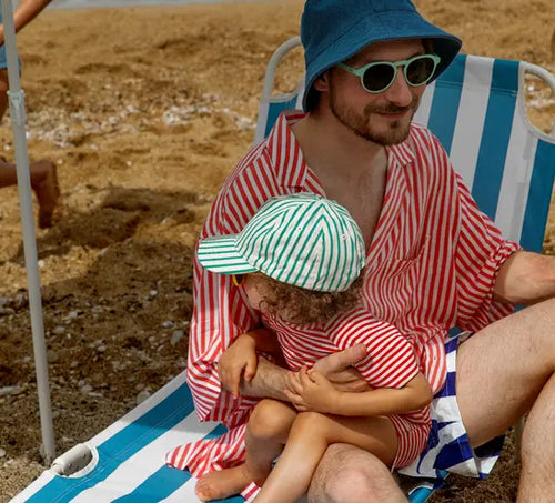 Pai abraça carinhosamente seu filho. Ambos estão em uma cadeira na praia. - Mustela Brasil - 1